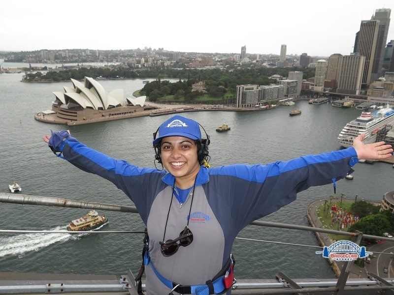 a girl posing at the top of Sydney Harbour bridge with a background of Sydney opera house